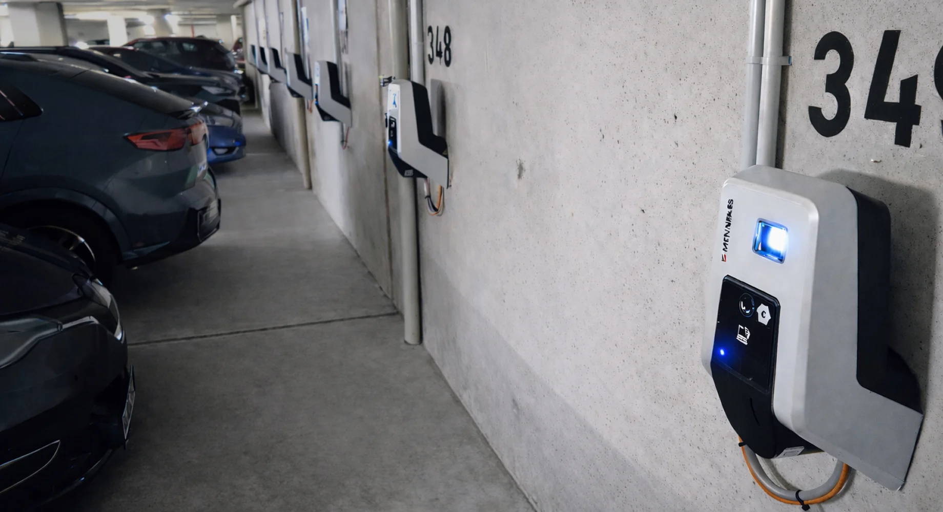Wandmontierte Ladestationen für Elektroautos in einer Tiefgarage neben parkenden Fahrzeugen