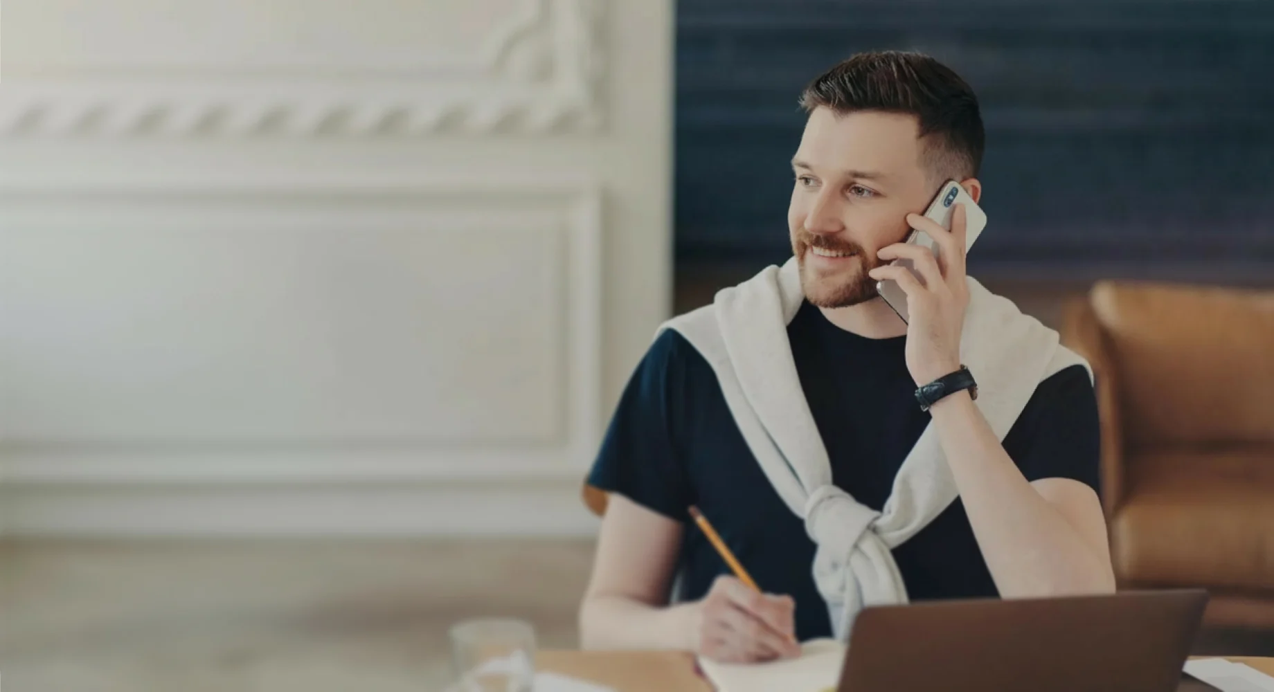 Mann telefoniert am Schreibtisch und schreibt Notizen neben einem Laptop