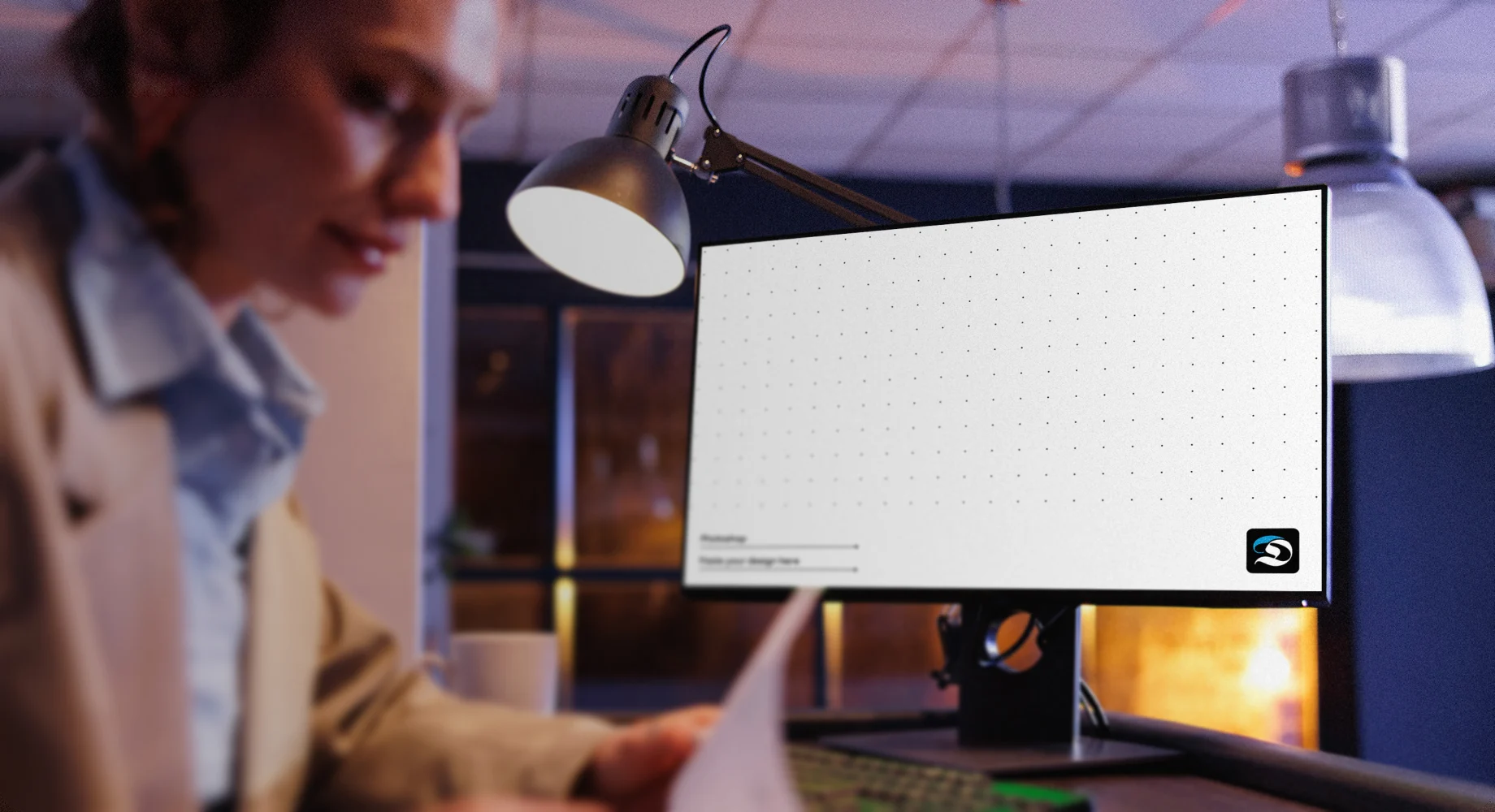 Frau arbeitet an einem Schreibtisch mit Monitor und Unterlagen im Buero