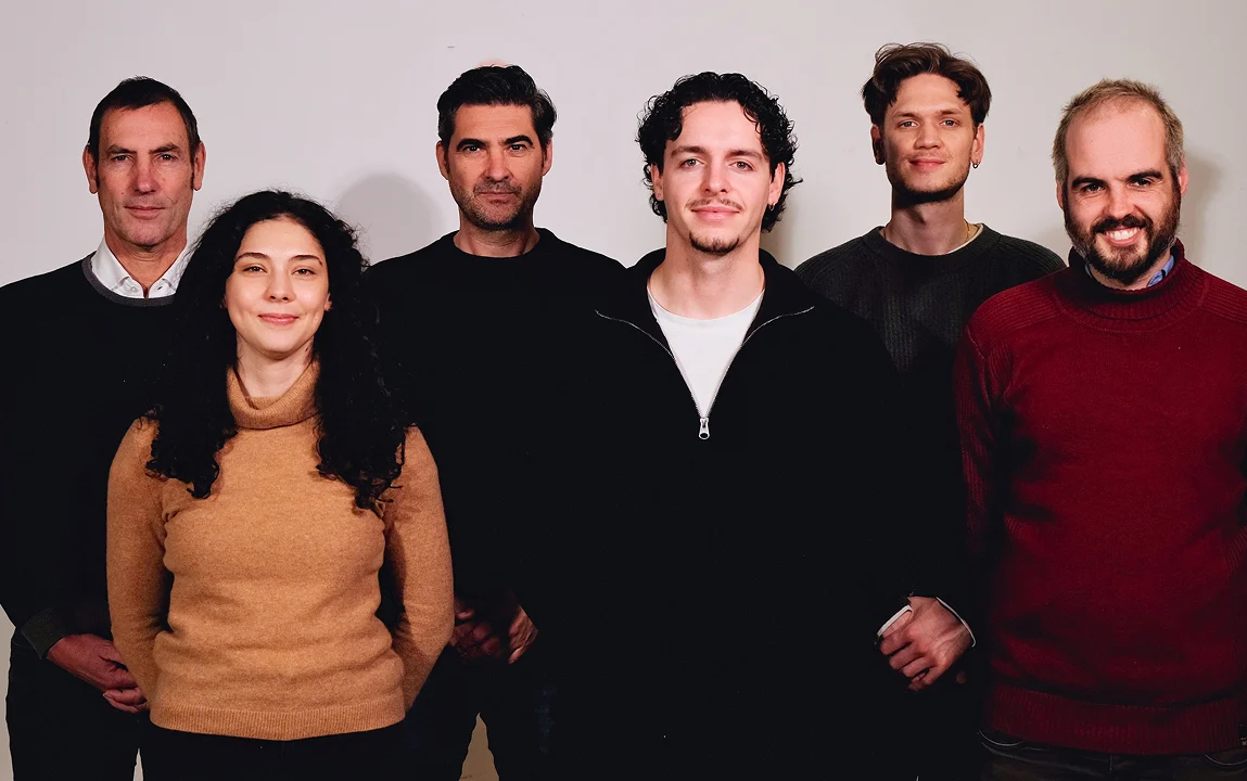 Mehrere Teammitglieder stehen nebeneinander vor einer hellen Wand und blicken in die Kamera