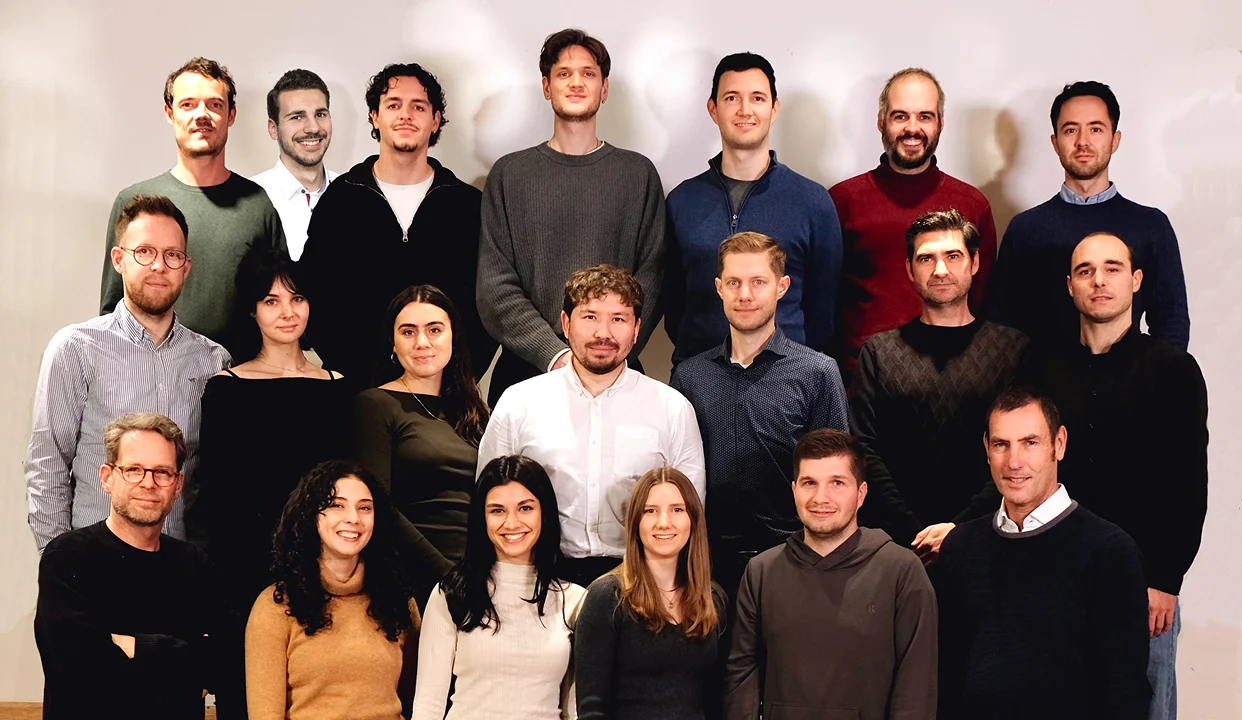 Gesamtteam von Frequentum steht in mehreren Reihen vor einer hellen Wand und blickt in die Kamera