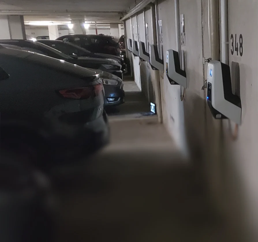 Reihe wandmontierter Ladestationen für Elektroautos in einer Tiefgarage neben parkenden Fahrzeugen