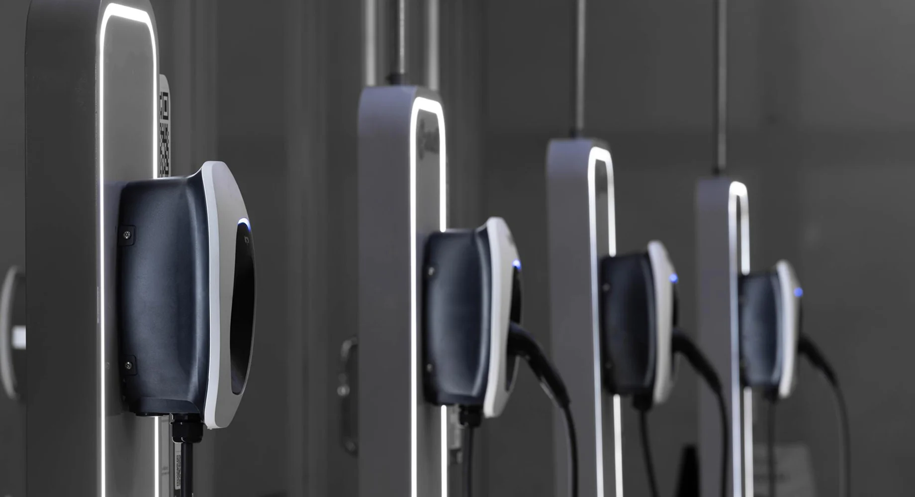 Mehrere wandmontierte Ladestationen für Elektroautos mit angeschlossenen Ladekabeln in moderner Innenumgebung