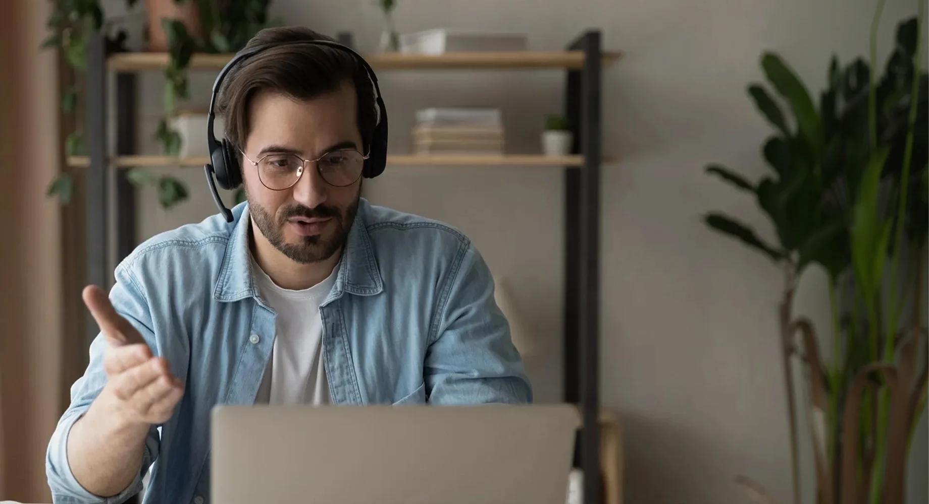 Mann mit Headset spricht in einem Online Webinar vor einem Laptop in einem Homeoffice