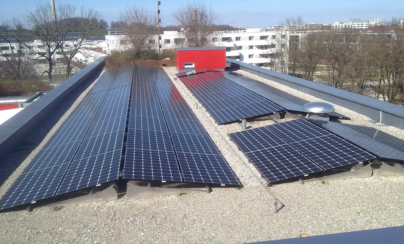 Photovoltaikanlage mit Solarmodulen auf einem Flachdach, Wohngebäude und Bäume im Hintergrund
