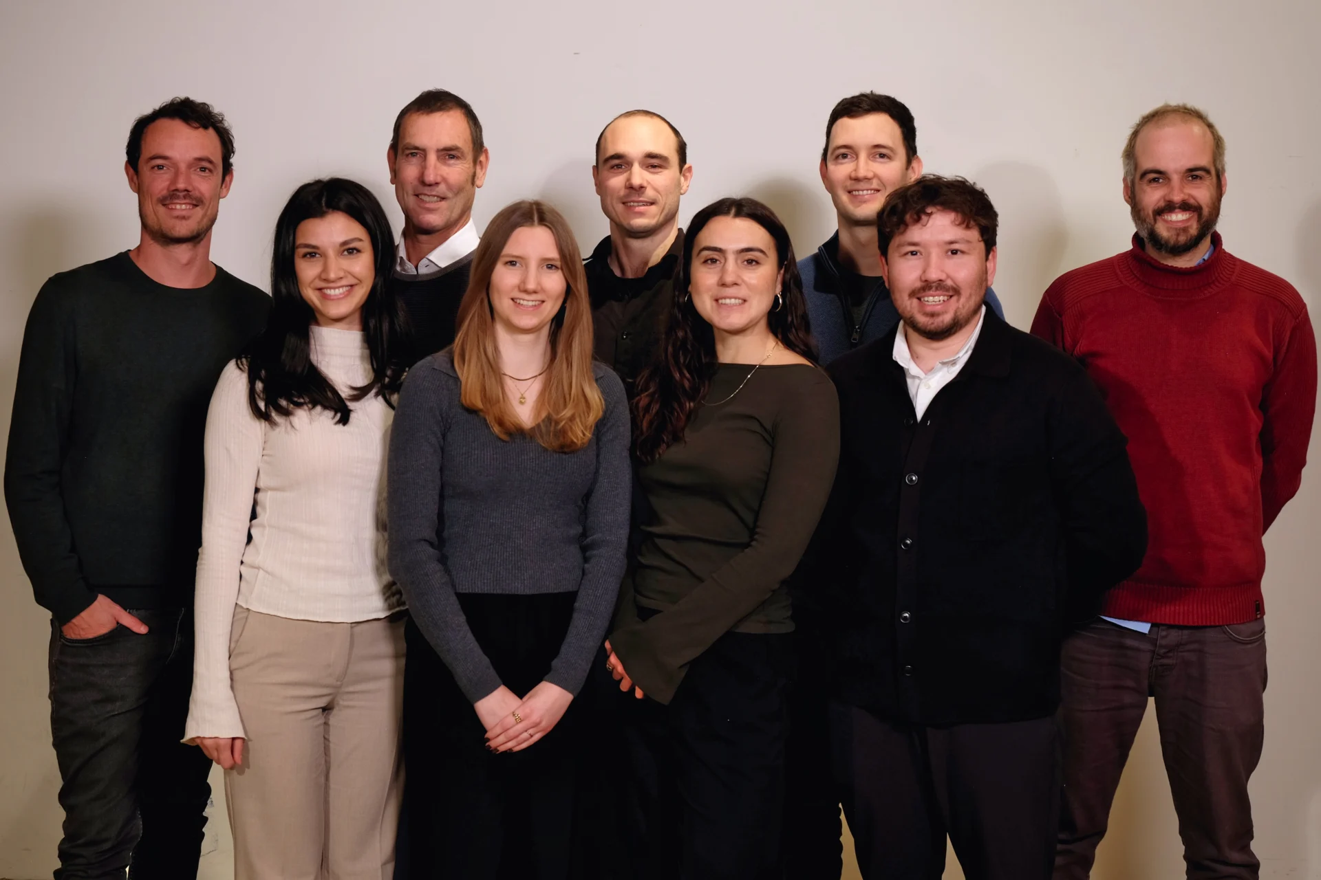 Mehrere Teammitglieder stehen nebeneinander vor einer hellen Wand und blicken in die Kamera